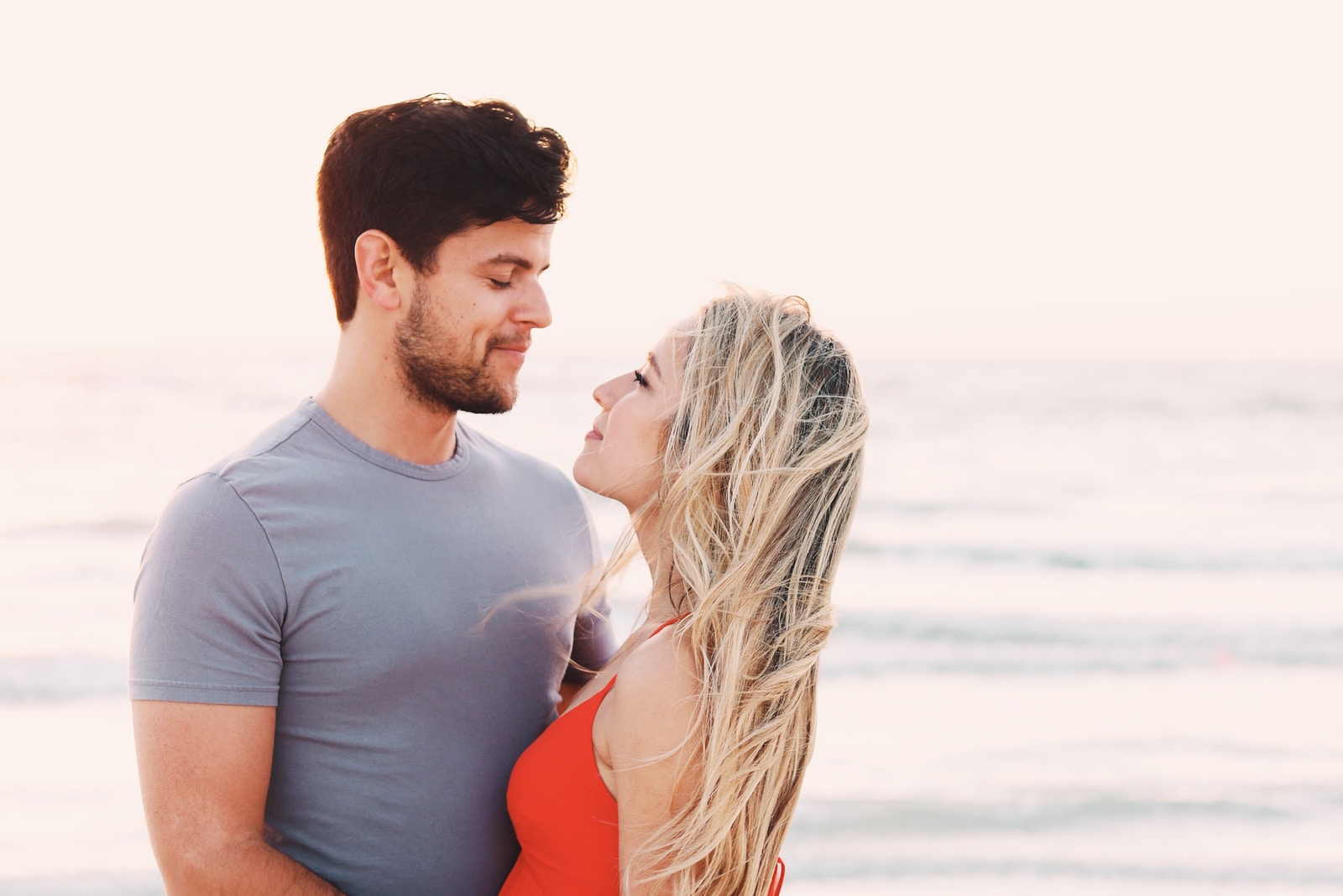 man wearing blue crew-neck top and woman wearing orange spaghetti strap top standing seashore